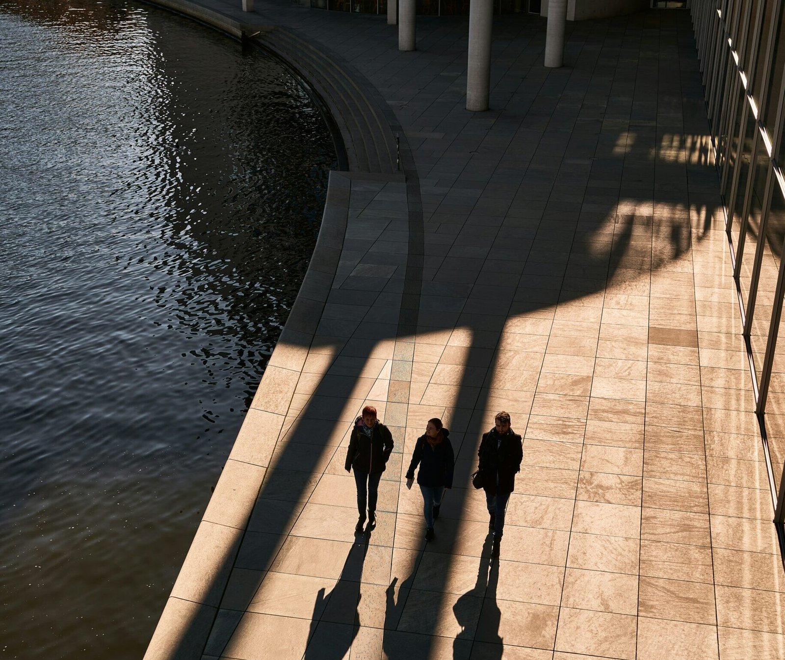 a group of people walking down a sidewalk next to a body of water